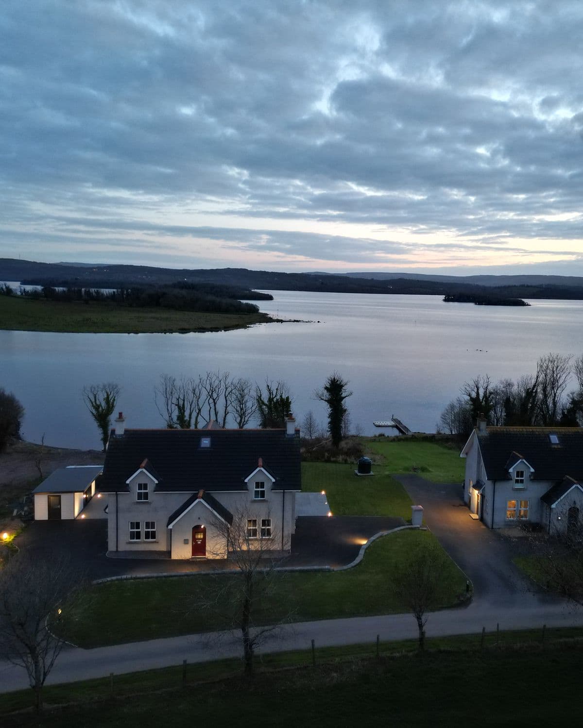 Two holiday homes managed by Escape Ordinary on the shore of Lough Erne, Fermanagh, lit up at dusk